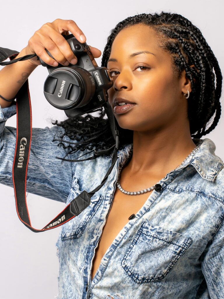 Confident woman with braided hair holding a camera in a studio setting.