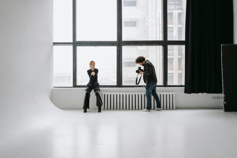 Photographer capturing model in modern studio with large windows and minimal decor.